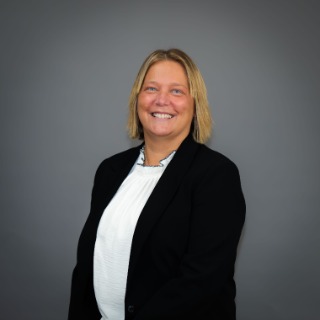 Short blonde-haired woman wearing a white shirt and black blazer jacket