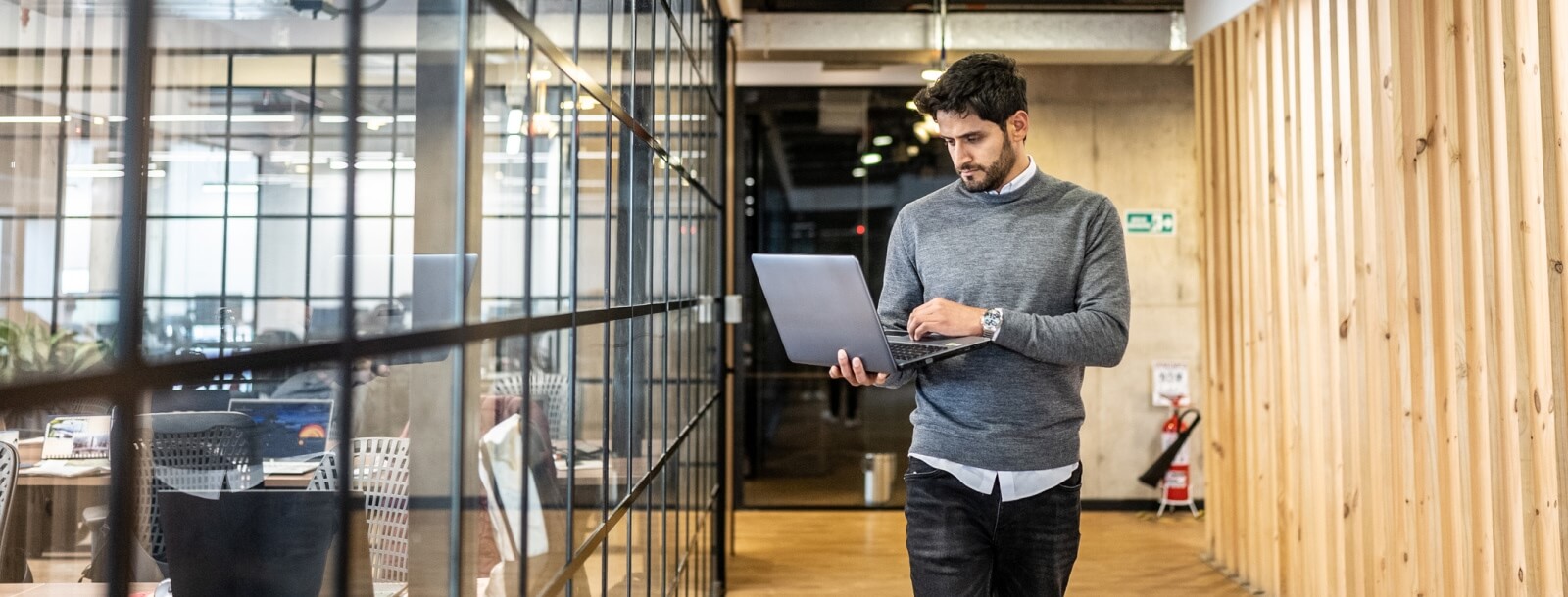 Young man walking in an office with a laptop